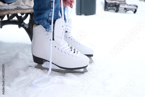 A woman sitting on a bench in the park puts on figure skates and ties her shoelaces with her hands, close-up view photo