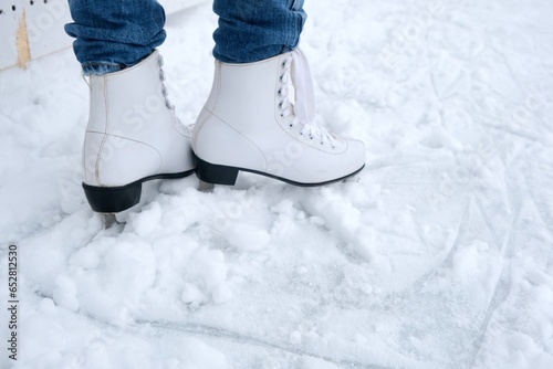 A woman sitting on a bench in the park puts on figure skates and ties her shoelaces with her hands, close-up view
