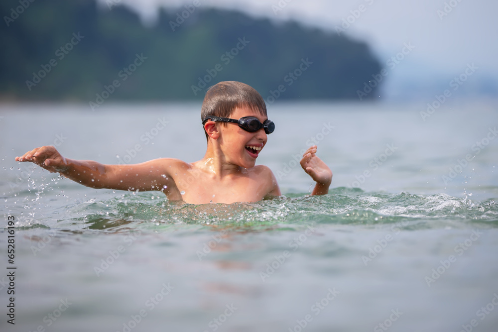 A boy in swimming goggles swims in the sea.