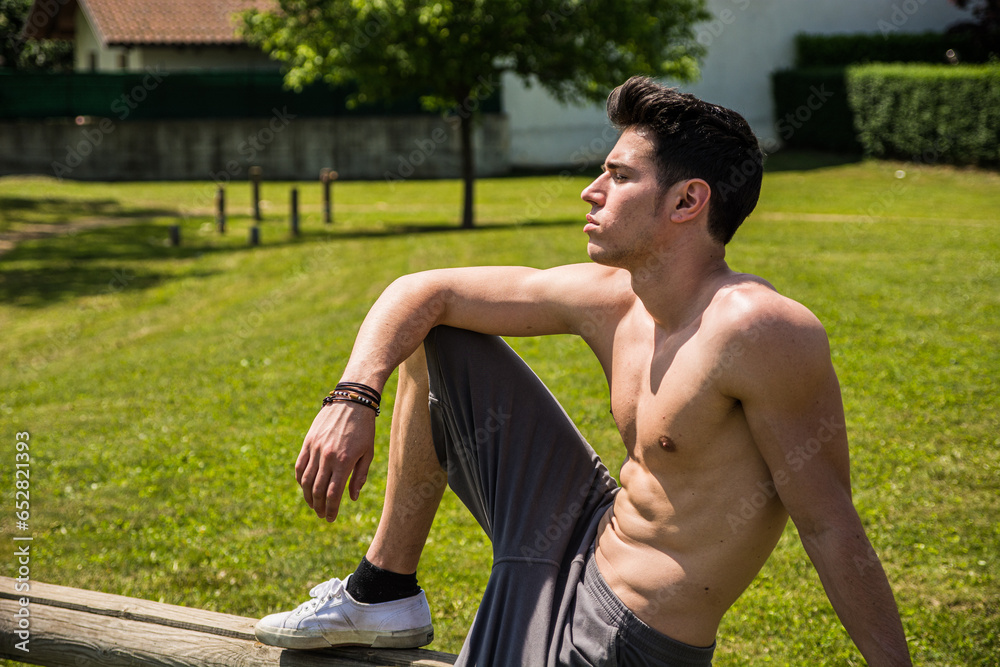 Obraz premium A shirtless man sitting on a bench in a park. Photo of a man enjoying a peaceful moment on a park bench