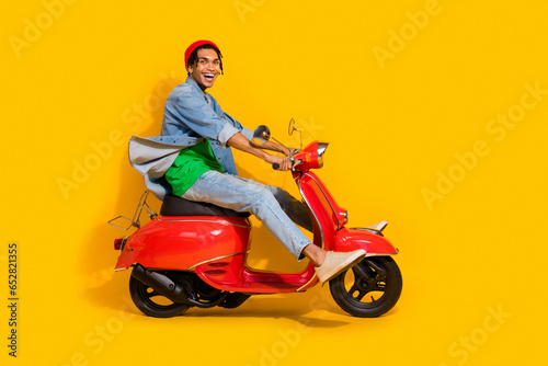 Full size photo of nice young guy driving red vintage scooter moped excited wear trendy jeans outfit isolated on yellow color background © deagreez