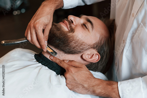 On the neck, shaving the beard. Man is visiting modern barber shop. Modern style