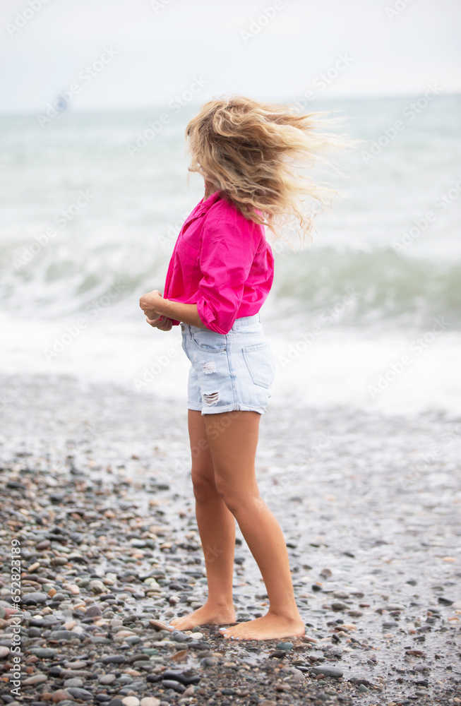 Beautiful woman on the background of the sea in denim shorts and a bright shirt. Beautiful woman on the background of the sea in denim shorts and a bright shirt.