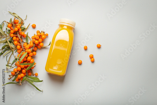 Sea buckthorn healthy juicy drink in bottle and branches with leaves and ripe berries top view on light grey simple background. Space for text..