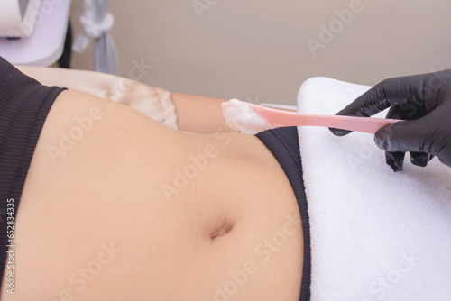 Closeup shot of using a cosmetic spatula to spread RF cream to a patients abdomen prior to a Radiofrequency skin tightening or fat reduction treatment. At a dermatologist or aesthetic clinic. photo