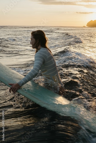 Female with a surfboard in the ocean © Polina Kuzovkova/Wirestock Creators