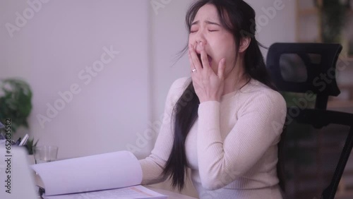 sleepy tired young Asian woman working on laptop computer her eyes are closing and she is about to fall asleep feeling uninterested demotivated at home. photo