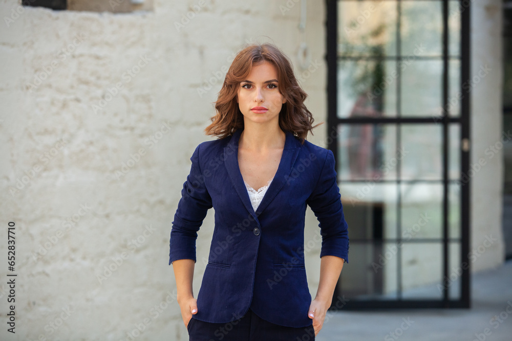 Portrait of a successful business woman in front of modern business building. Young manager poses outside. Woman employee of an office.