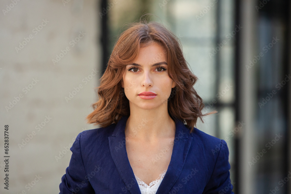 Portrait of a successful business woman in front of modern business building. Young manager poses outside. Woman employee of an office. Portrait of a successful business woman in front of modern business building. Young manager poses outside. Woman employee of an office.