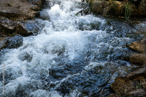 A stormy stream of a mountain river flows over large and small stones, white waves, strong current, small waterfalls, swirls, dark water