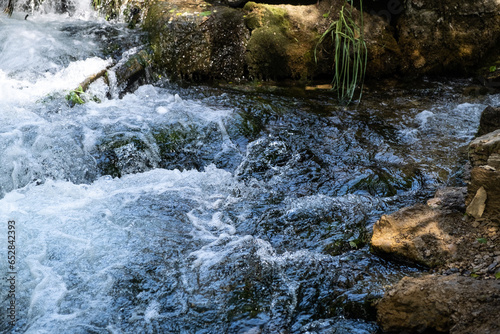 A stormy stream of a mountain river flows over large and small stones, white waves, strong current, small waterfalls, swirls, dark water