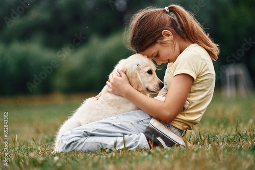 On the ground. Cute little girl is with golden retriever dog on the field