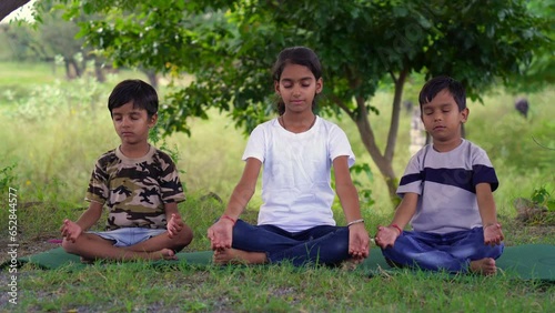 Group Of Indian Children or Kids Sitting On Exercise Mats And Meditating In Yoga Garden
