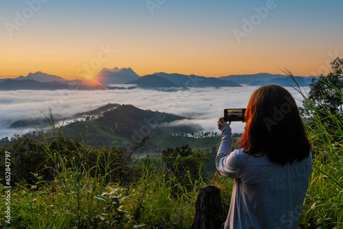 Female tourists backpacks, travel, hike, hold smartphones to take pictures of the scenery and admire the sea of mist from the mountain top and feeling free, good weather in the morning, weekend 