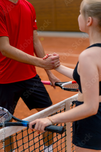 young man and woman shaking hands before the start of a tennis game on an open court sports players opponents close-up