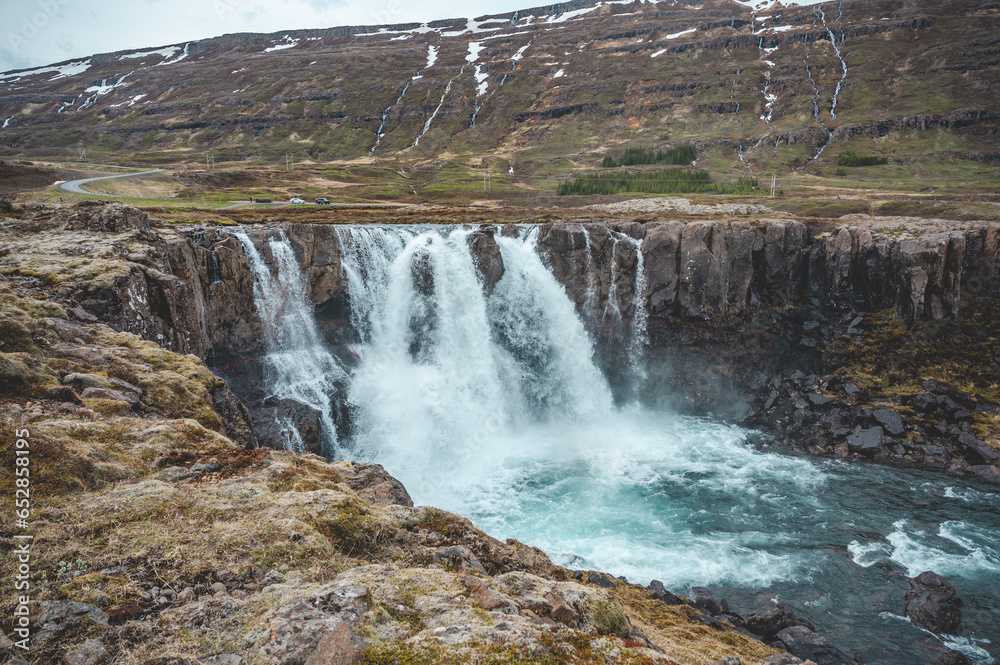 Fototapeta premium Beautiful Waterfall at Seydisfjordur, Iceland with snow mountains in the background