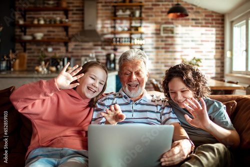 Grandfather video calling with his grandchildren on the couch at home photo