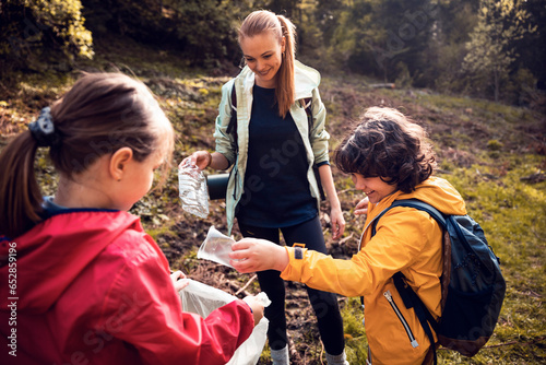 Young Caucasian mother and her children cleaning and recycling plastic while hiking in the woods photo