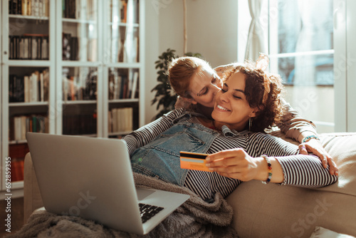 Young lesbian couple online shopping for their future child on the couch at home photo