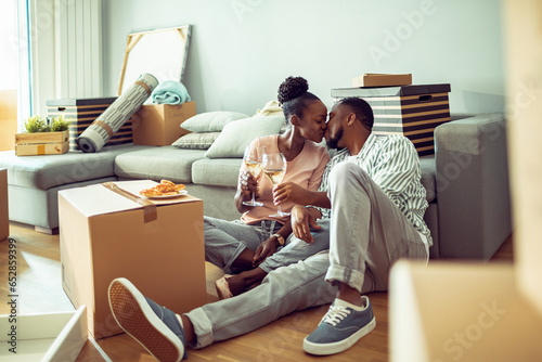 Young African American couple taking a break from moving in to have wine and snacks in their new apartments living room