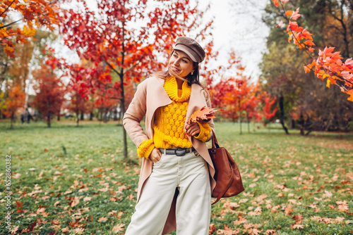 Stylish woman wears yellow sweater holding handbag in autumn park. Warm fall female clothes and accessories. Fashion