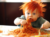 Red-haired baby boy eating spaghetti in the kitchen. 