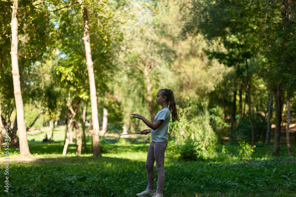 little cute caucasian girl, playing badminton in a summer park, surrounded by green trees little cute caucasian girl, playing badminton in a summer park, surrounded by green trees
