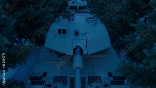An aerial view over an armored military tank platoon taking cover at night under the spruce trees of a snow-covered road.