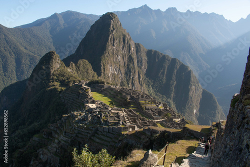 Panorama of Machupicchu with view of the mountains and archeological site, along with a stone staircase to the ruins with silhouettes of people descending it, in Peru, Sacred Valley. 