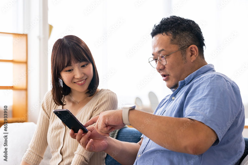 Fototapeta premium リビングでスマートフォンを使う男女