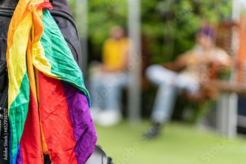 image of a detail of the diversity flag hanging on a bag with two people out of focus in the background representing the lgbt community.