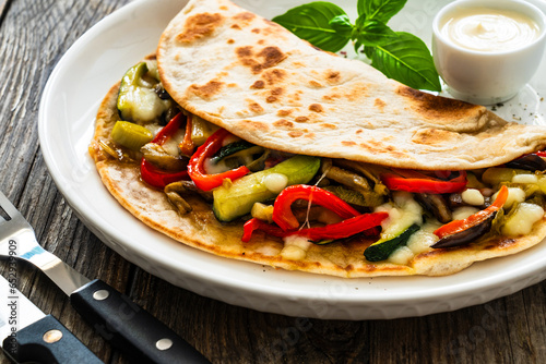 Italian piada wraps - piadina filled with fried vegetables and mozzarella cheese on wooden table

