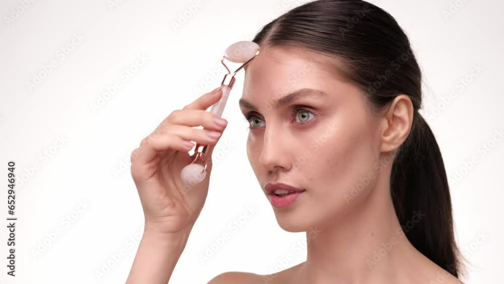 Beautiful female using natural massager tool for skin care and spa beauty treatment closeup portrait. Young woman using jade facial roller for face massage smiling and look at the camera. Slow motion. Beautiful female using natural massager tool for skin care and spa beauty treatment closeup portrait. Young woman using jade facial roller for face massage smiling and look at the camera. Slow motion.