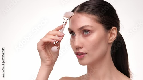 Beautiful female using natural massager tool for skin care and spa beauty treatment closeup portrait. Young woman using jade facial roller for face massage smiling and look at the camera. Slow motion.