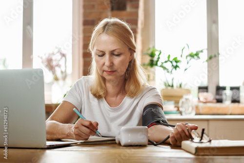 Senior woman measuring her blood pressure. Retired uses medicine digital device tonometer for control health at home