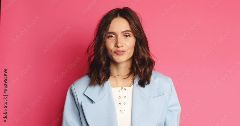 A positive young woman is nodding while listening the viewer standing isolated over a pink wall in the studio.