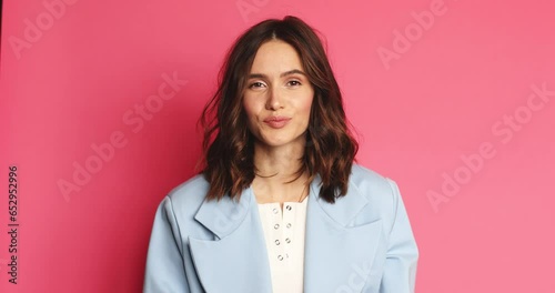 A positive young woman is nodding while listening the viewer standing isolated over a pink wall in the studio.