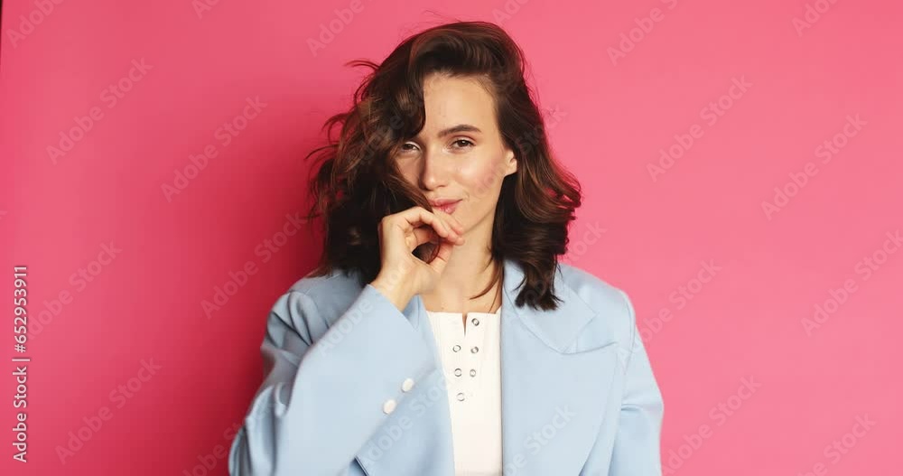 Lovely coquettish brunette woman, winking playfully, flirting. Woman fix her hair isolated on pink background. Curly hair fashion model face smiling. Girl look at camera. Lovely coquettish brunette woman, winking playfully, flirting. Woman fix her hair isolated on pink background. Curly hair fashion model face smiling. Girl look at camera.