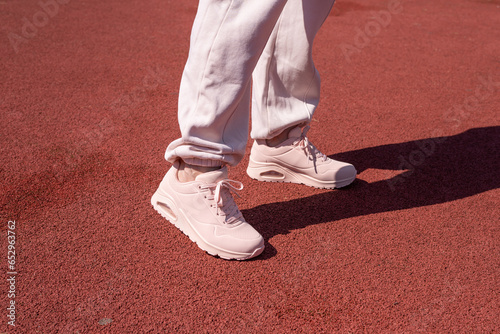 Woman legs in sports wear and pink sneakers standing on a tartan path in a park