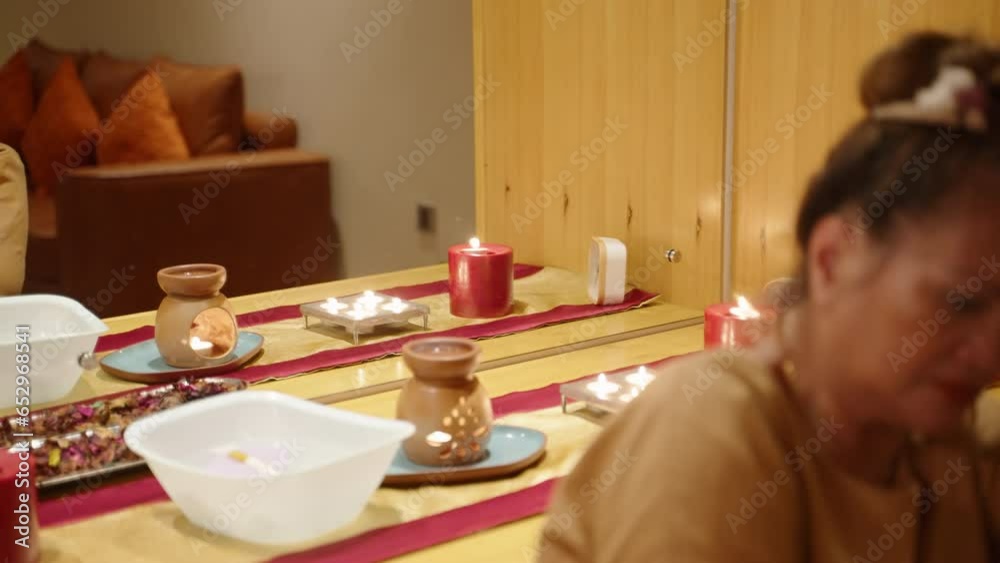 Focused senior asian female spa center worker giving a procedure to a client portrait shot unfocused. Closeup of a biethnic elderly masseuse at wellness facility. Candles, flowers and beauty tools Focused senior asian female spa center worker giving a procedure to a client portrait shot unfocused. Closeup of a biethnic elderly masseuse at wellness facility. Candles, flowers and beauty tools