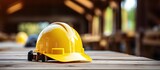 Blurry background shows architects yellow and white hard safety helmet on wooden desk