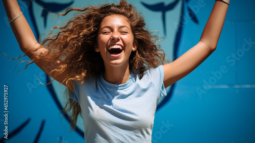 Against a bold blue backdrop, an ecstatic schoolgirl, donning a stylish t-shirt, clutches a football in triumph. Her elation radiates from the image, capturing the sheer joy of vic photo