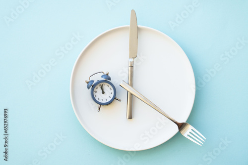 Intermittent fasting concept. Healthy eating, diet. White plate with cutlery and clock.