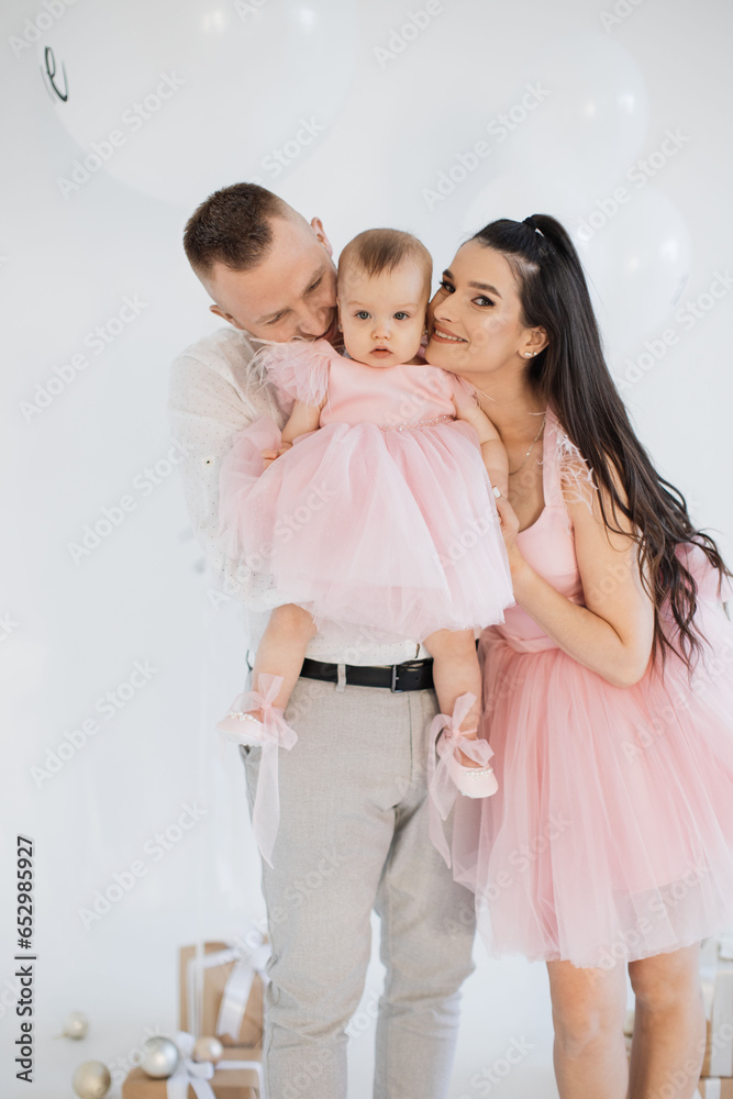 Cheerful spouse in stylish clothes hugging with love pretty baby girl at decorated studio. Joyful family of father, mother and little daughter sharing happy moments of birthday celebration. Cheerful spouse in stylish clothes hugging with love pretty baby girl at decorated studio. Joyful family of father, mother and little daughter sharing happy moments of birthday celebration.