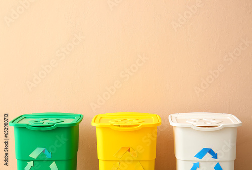 Different garbage bins with recycling symbol near beige wall
