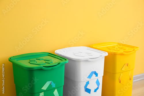 Different garbage bins with recycling symbol near yellow wall