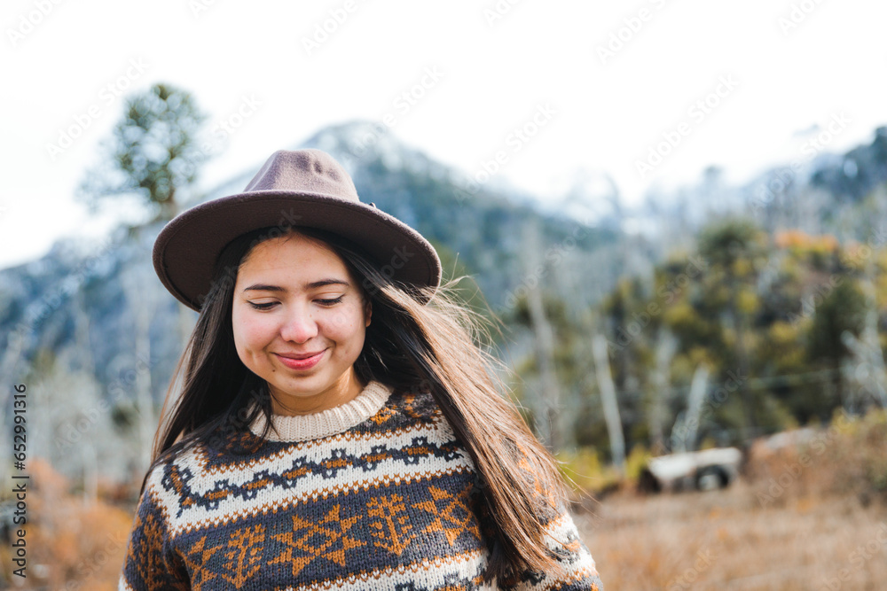 Candid portrait of a young latin woman, wearing cozy attire and a hat, enjoying the mountain, contemplating the forest