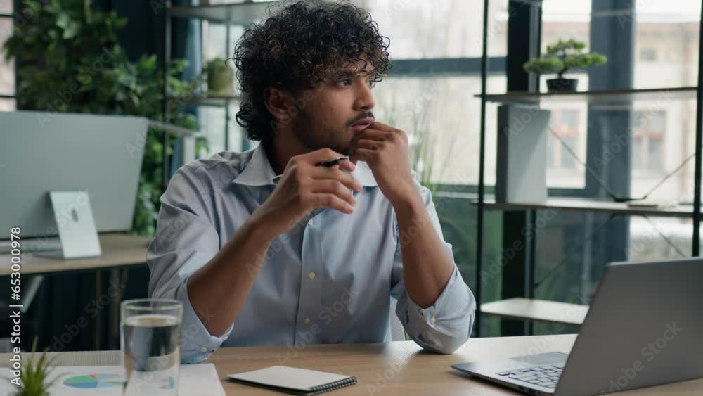 Thoughtful pensive Arabian businessman working with laptop at office desk doubtful Indian Hispanic man looking away creative mind think idea solve problem solution create business plan search answer