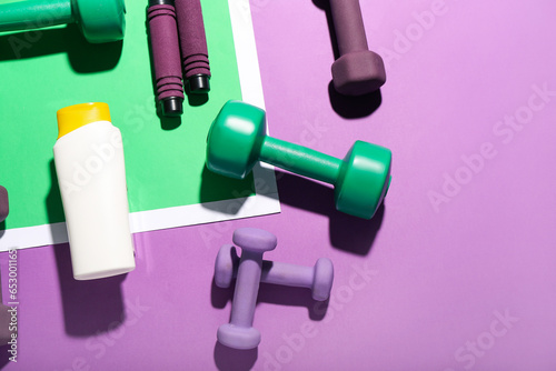Composition with bottle of sunscreen cream, dumbbells and skipping rope on color background