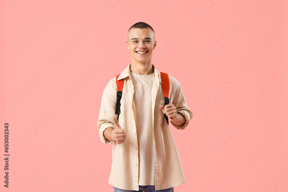 Happy male student with backpack showing thumb-up gesture on pink background - obrazy, fototapety, plakaty 